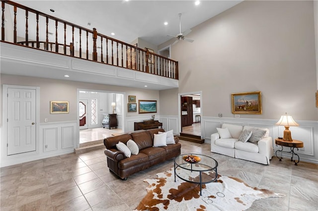 living area with a ceiling fan, recessed lighting, a decorative wall, a wainscoted wall, and a towering ceiling