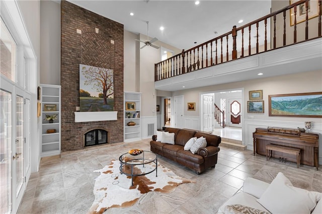 living room with a towering ceiling, recessed lighting, a fireplace, built in features, and a ceiling fan