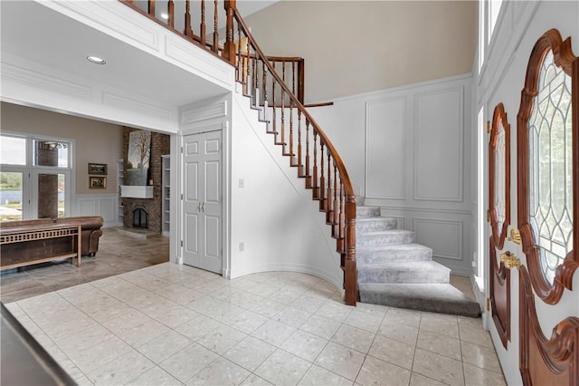 foyer entrance featuring a decorative wall, light tile patterned flooring, a high ceiling, and stairs