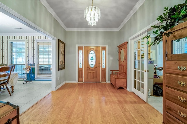 entrance foyer featuring a notable chandelier, ornamental molding, a wealth of natural light, and light hardwood / wood-style flooring