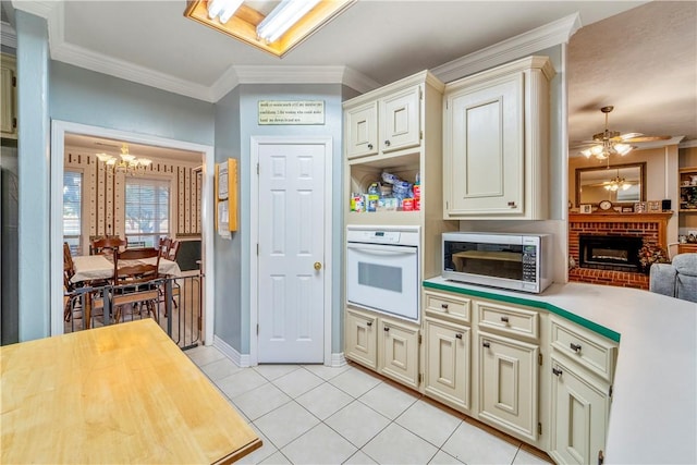 kitchen with a brick fireplace, crown molding, oven, light tile patterned floors, and ceiling fan with notable chandelier