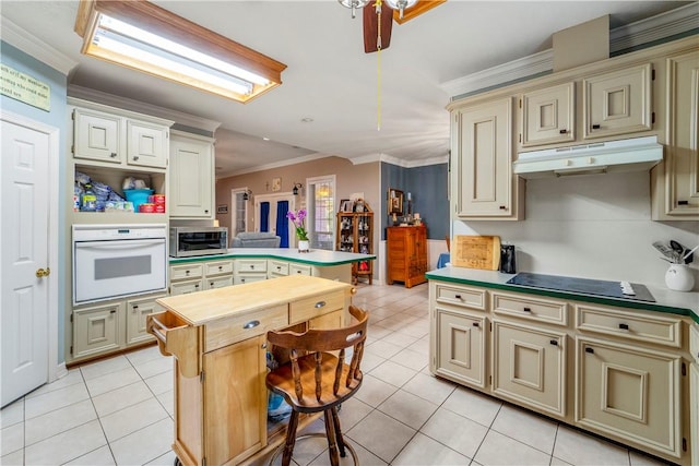 kitchen with white oven, crown molding, cream cabinets, light tile patterned floors, and a kitchen island