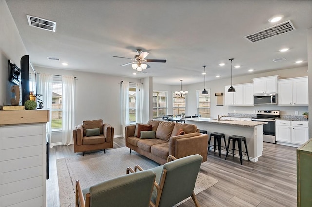 living room featuring ceiling fan with notable chandelier, sink, and light hardwood / wood-style flooring