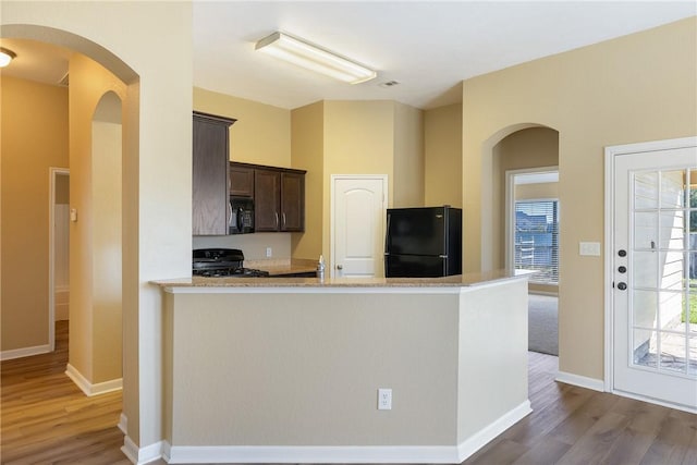 kitchen featuring wood-type flooring, black appliances, kitchen peninsula, sink, and dark brown cabinets