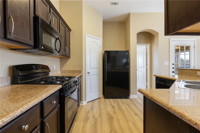 kitchen with light stone countertops, light hardwood / wood-style floors, black appliances, dark brown cabinets, and sink