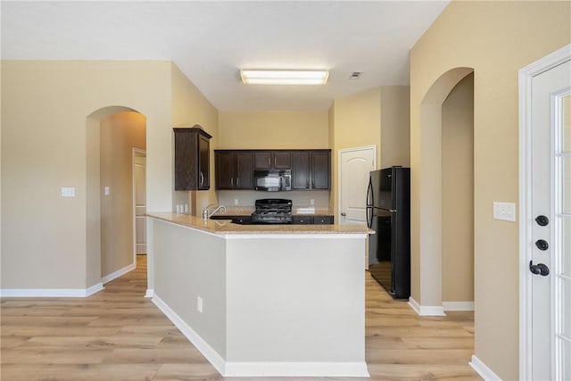 kitchen with light wood-type flooring, kitchen peninsula, dark brown cabinetry, light stone countertops, and black appliances