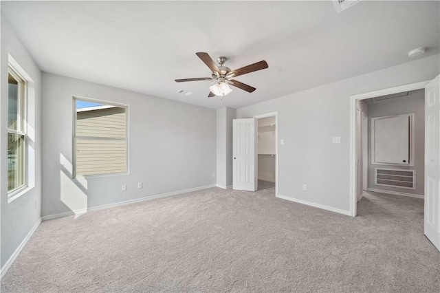 unfurnished bedroom with ceiling fan, a closet, light colored carpet, and a walk in closet