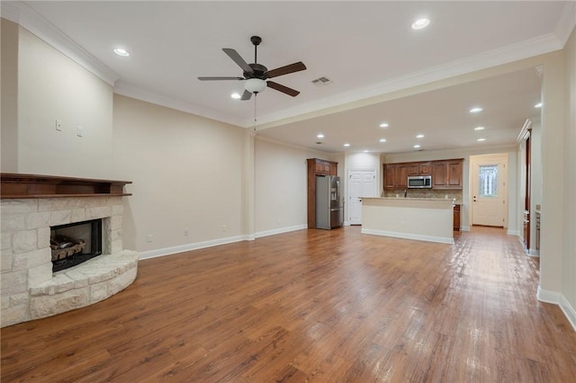 unfurnished living room featuring ceiling fan, light hardwood / wood-style floors, a stone fireplace, and ornamental molding