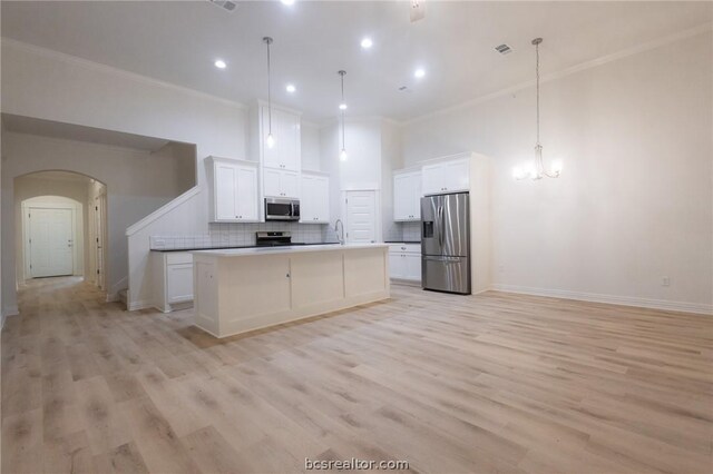 kitchen with appliances with stainless steel finishes, backsplash, a kitchen island with sink, decorative light fixtures, and white cabinetry