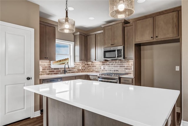 kitchen with a center island, backsplash, sink, hanging light fixtures, and appliances with stainless steel finishes