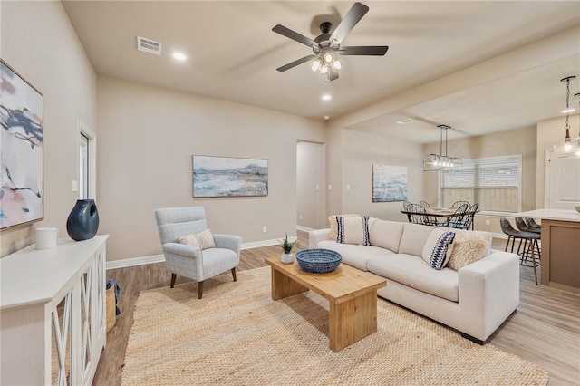 living room with ceiling fan with notable chandelier and light hardwood / wood-style floors