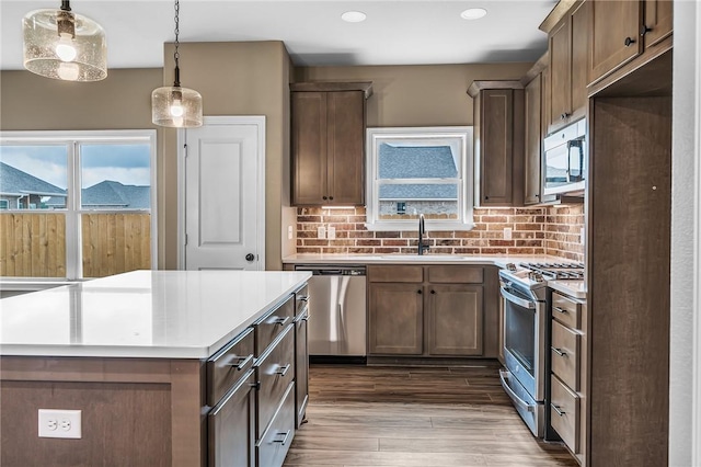 kitchen featuring sink, appliances with stainless steel finishes, backsplash, a kitchen island, and decorative light fixtures