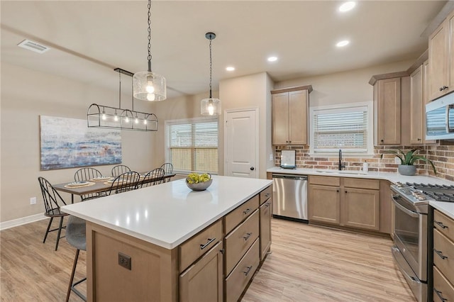 kitchen with pendant lighting, sink, stainless steel appliances, light hardwood / wood-style floors, and a kitchen island