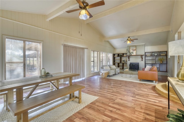 living room featuring a wood stove, high vaulted ceiling, ceiling fan, beam ceiling, and light hardwood / wood-style floors