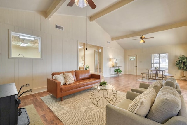 living room with wood-type flooring, lofted ceiling with beams, ceiling fan, and wooden walls