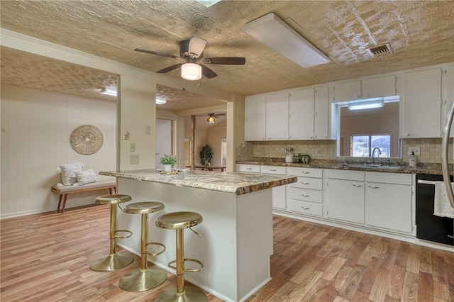 kitchen featuring white cabinets, wooden walls, light stone countertops, light wood-type flooring, and a textured ceiling