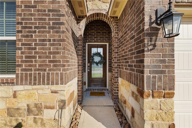 view of exterior entry featuring brick siding and a garage