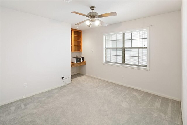 carpeted empty room with built in desk and ceiling fan