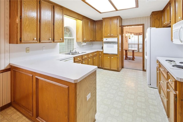 kitchen with white appliances, an inviting chandelier, sink, wooden walls, and kitchen peninsula