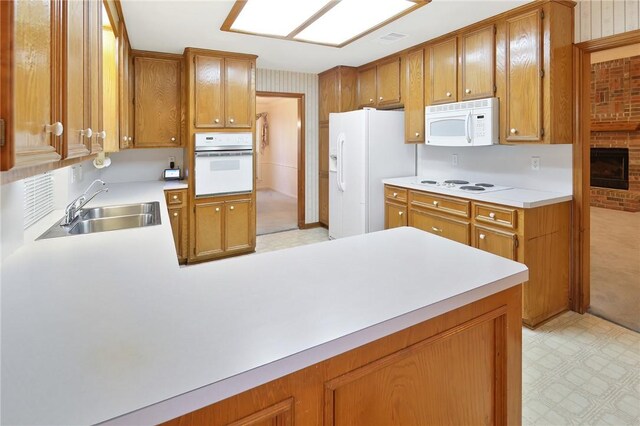 kitchen featuring kitchen peninsula, white appliances, a fireplace, and sink