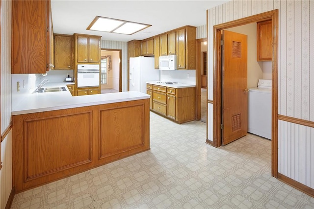 kitchen with kitchen peninsula, washer / dryer, white appliances, and sink