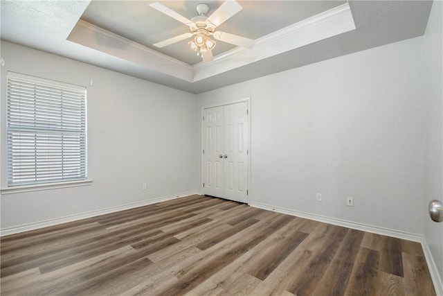 spare room featuring a tray ceiling, ornamental molding, ceiling fan, wood finished floors, and baseboards