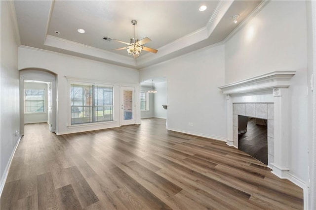 unfurnished living room with arched walkways, a fireplace, wood finished floors, ornamental molding, and a raised ceiling