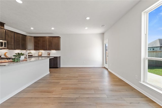 kitchen featuring light stone countertops, dark brown cabinetry, and light hardwood / wood-style flooring