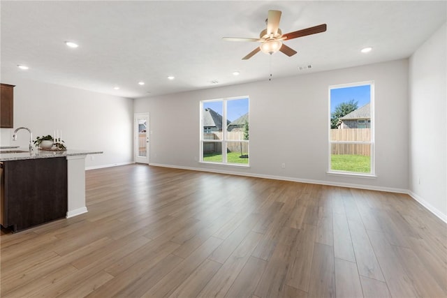 unfurnished living room featuring plenty of natural light, ceiling fan, sink, and light hardwood / wood-style flooring