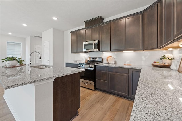 kitchen with light stone countertops, sink, stainless steel appliances, and light wood-type flooring