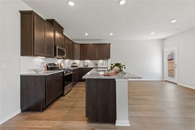 kitchen featuring appliances with stainless steel finishes, light stone counters, a kitchen island with sink, sink, and light hardwood / wood-style flooring