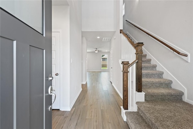 foyer featuring ceiling fan, light hardwood / wood-style flooring, and a towering ceiling