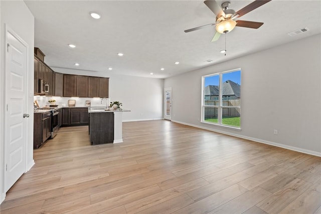 kitchen with light wood-type flooring, stainless steel appliances, ceiling fan, and an island with sink