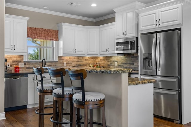 kitchen with white cabinets, appliances with stainless steel finishes, a kitchen breakfast bar, and dark stone countertops