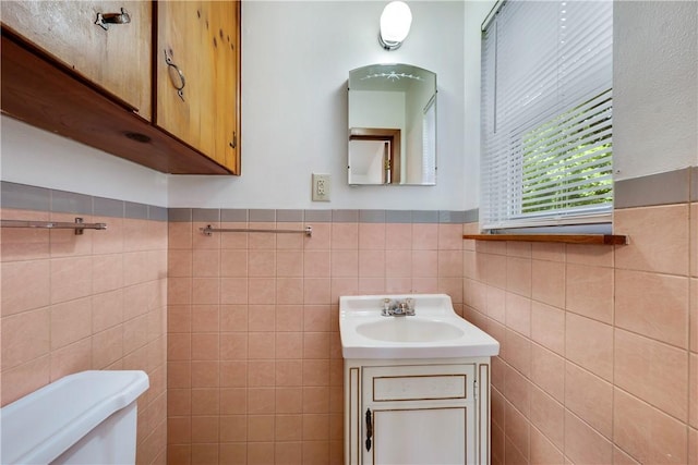 half bathroom featuring vanity, a wainscoted wall, toilet, and tile walls