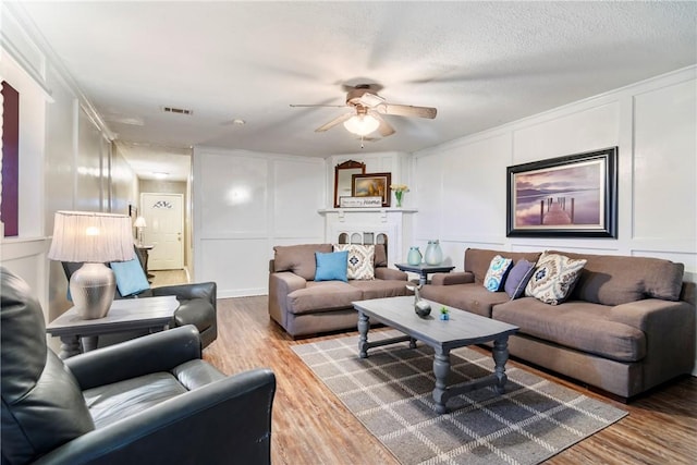 living room featuring a textured ceiling, wood finished floors, a fireplace, and a decorative wall