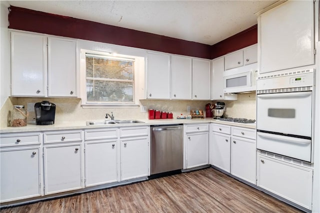 kitchen featuring white appliances, wood finished floors, a sink, light countertops, and a warming drawer