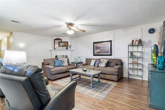 living area featuring light wood finished floors, visible vents, ceiling fan, a decorative wall, and a textured ceiling