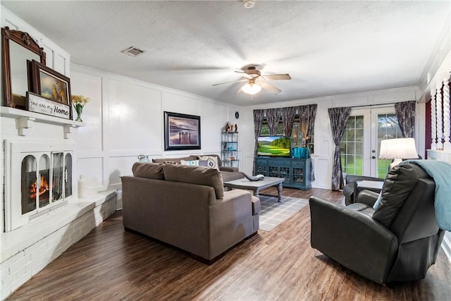 living area featuring visible vents, wood finished floors, french doors, a fireplace, and a decorative wall