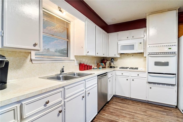 kitchen featuring white appliances, wood finished floors, a sink, light countertops, and a warming drawer