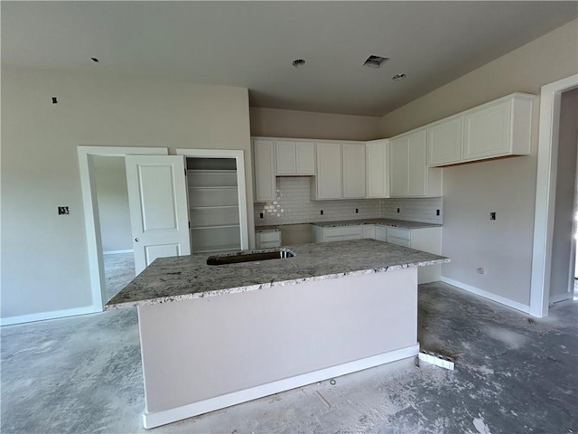 2814 Messenger Way, Bryan, TX 77802 - kitchen featuring unfinished concrete floors, a kitchen island, white cabinets, decorative backsplash, and light stone counters