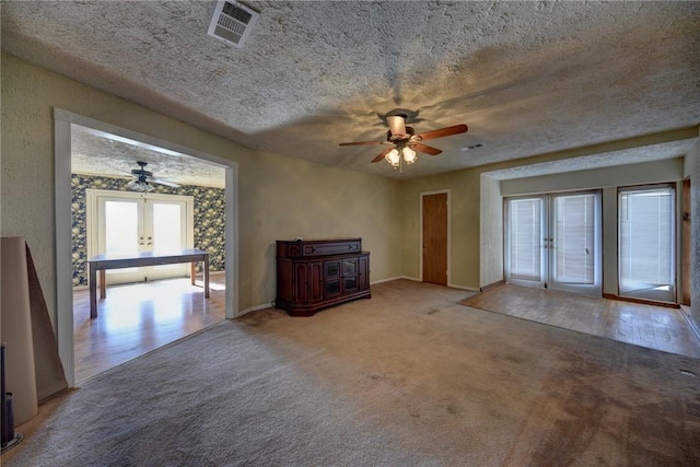 unfurnished living room with a textured ceiling, ceiling fan, french doors, and carpet