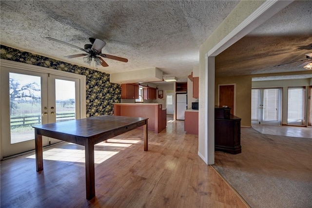 unfurnished dining area with light wood-type flooring, ceiling fan, french doors, and a textured ceiling