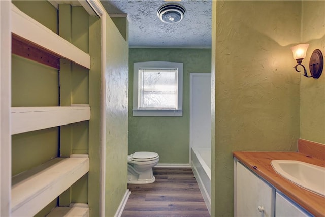 bathroom featuring a textured ceiling, hardwood / wood-style flooring, toilet, a washtub, and vanity