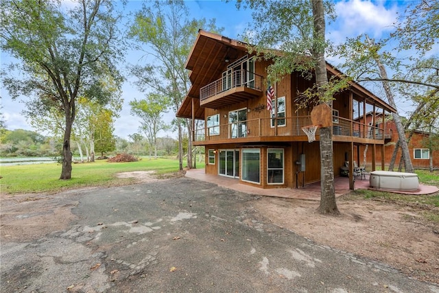 back of property featuring a patio, a hot tub, a balcony, and a lawn