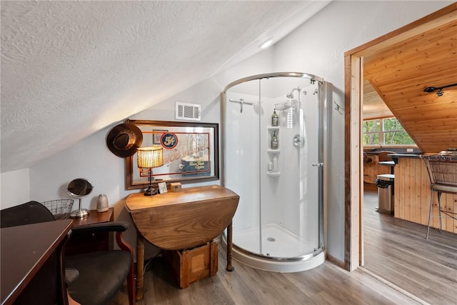 bathroom featuring wood-type flooring, a textured ceiling, vaulted ceiling, and walk in shower