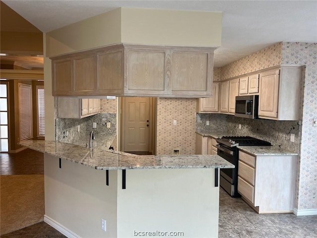 kitchen featuring light brown cabinetry, kitchen peninsula, appliances with stainless steel finishes, and a breakfast bar area