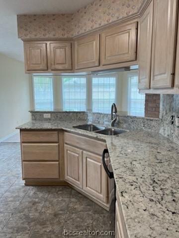 kitchen with light stone counters, kitchen peninsula, sink, and light brown cabinetry