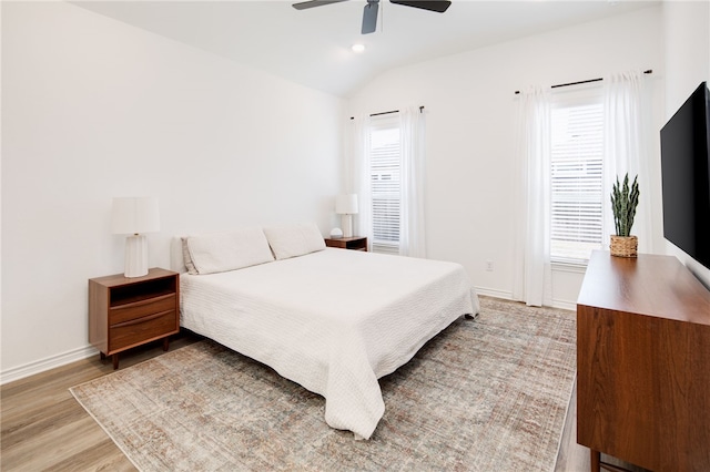 bedroom with multiple windows, vaulted ceiling, baseboards, and wood finished floors