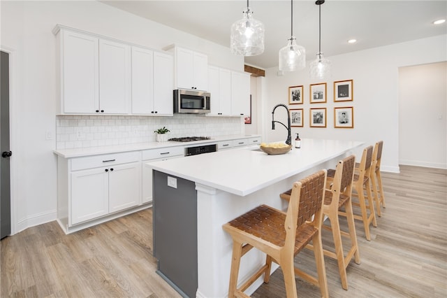 kitchen with light countertops, stainless steel microwave, a center island with sink, and white cabinets